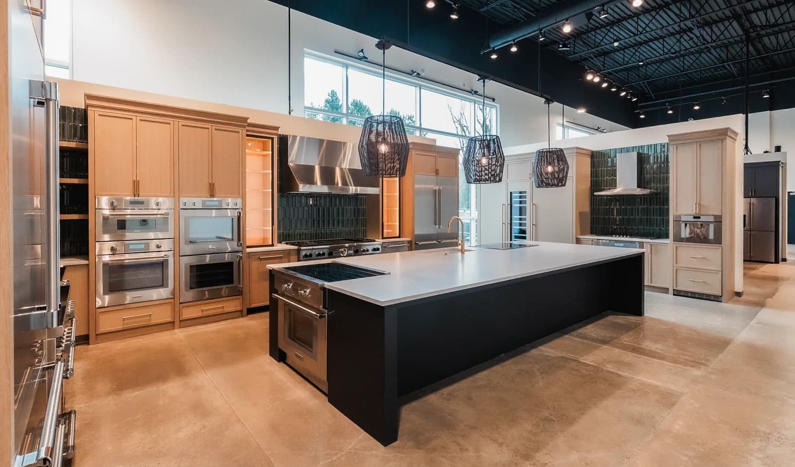 A showroom kitchen display with woven pendants over the island and track lighting across an open black ceiling