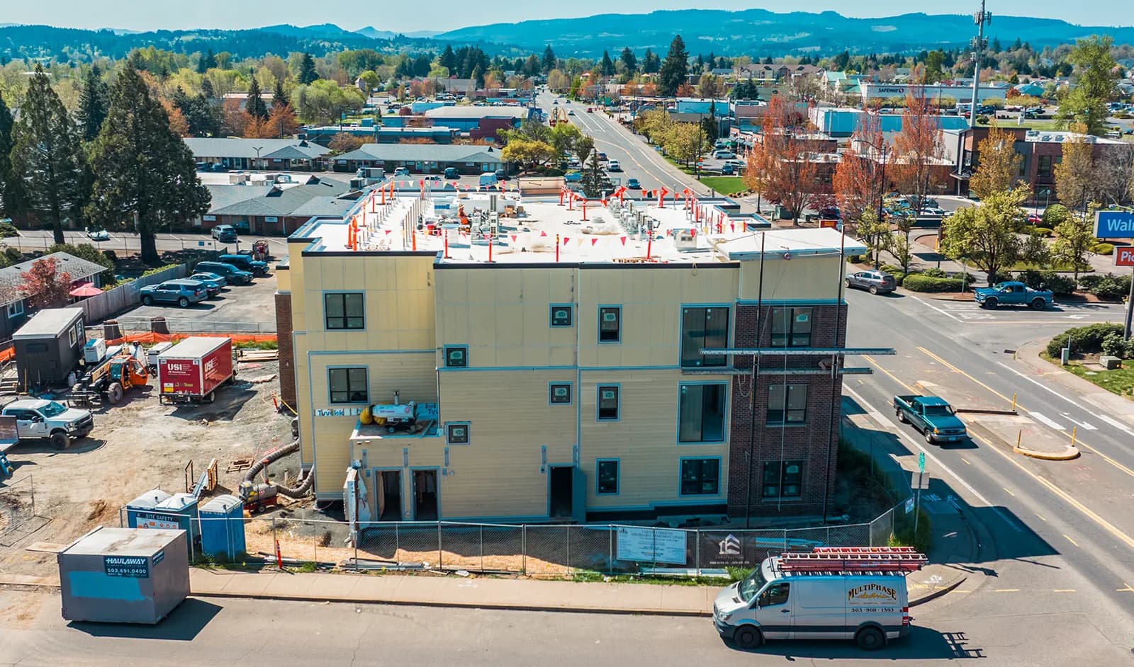 A three-storey mixed-use building under construction from above, rooftop equipment stubbed out and a service van at the kerb