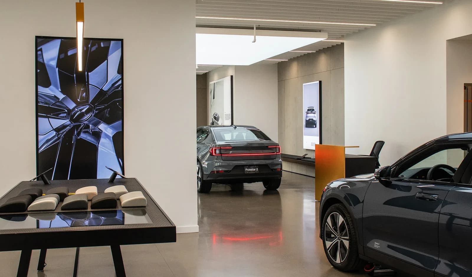 A showroom floor with cars under recessed and cove lighting, backlit display panels along the walls