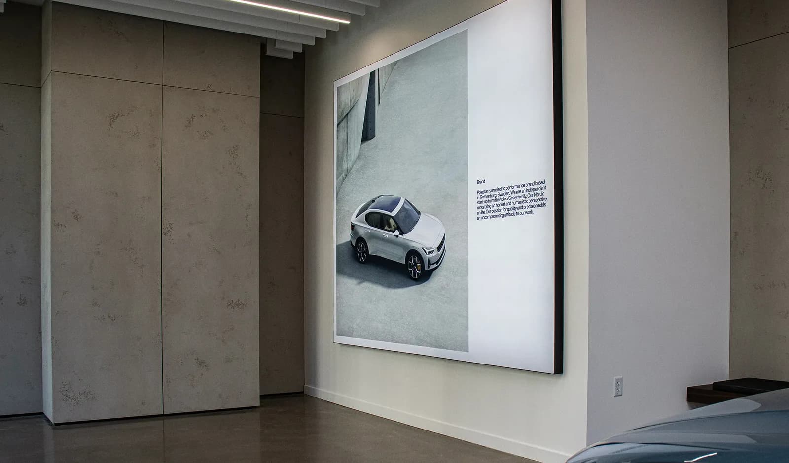 A large backlit lightbox display on a showroom wall, under a run of linear ceiling lighting