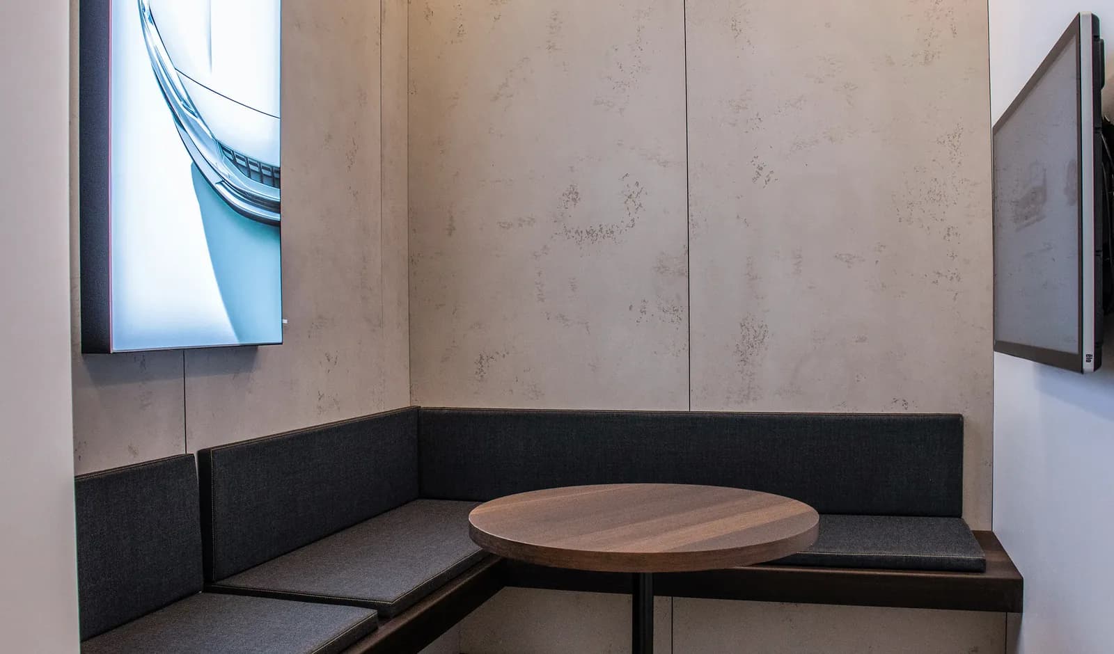 A seating nook in the showroom with banquette benches, a round table and a wall-mounted screen