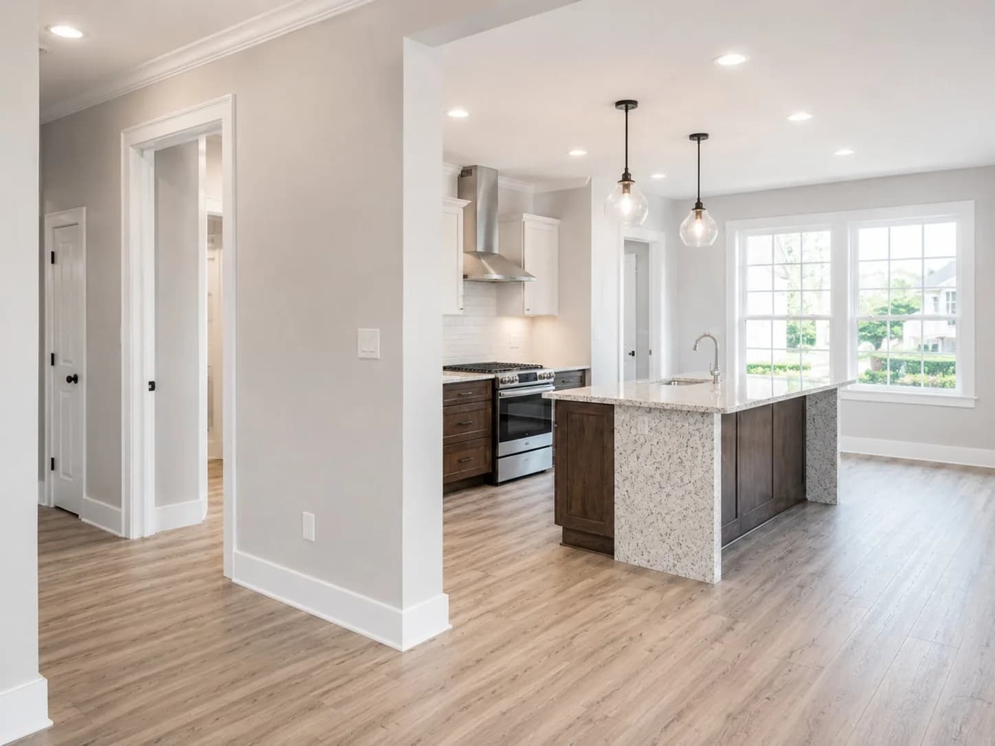 A finished open-plan kitchen and living space, lit by recessed downlights and two glass pendants over the island