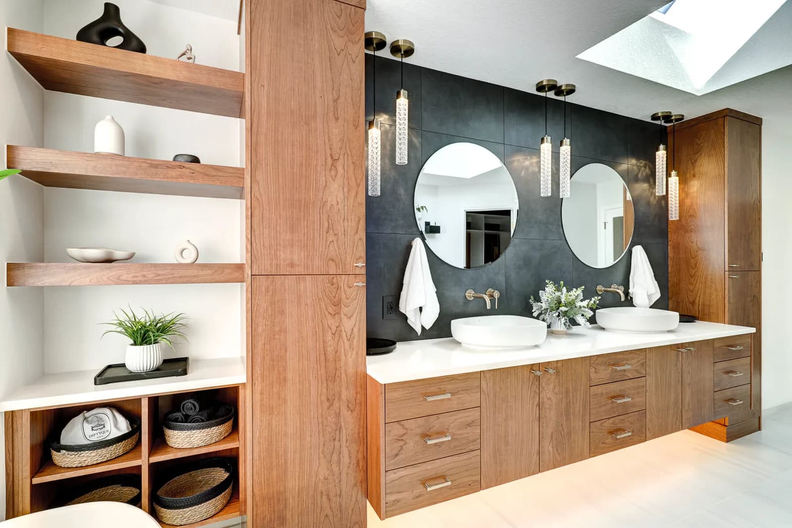 A double vanity with round mirrors, slim glass pendants either side and a skylight above