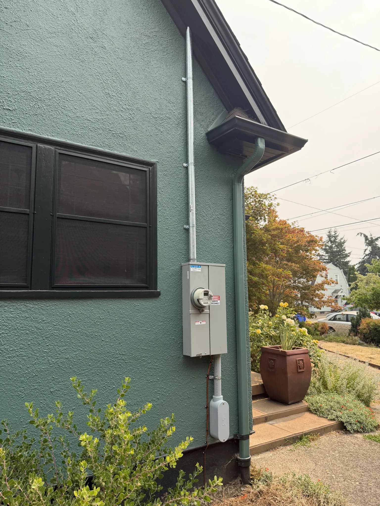 A meter base and service disconnect mounted on the teal stucco wall of a house, conduit running up to the roofline