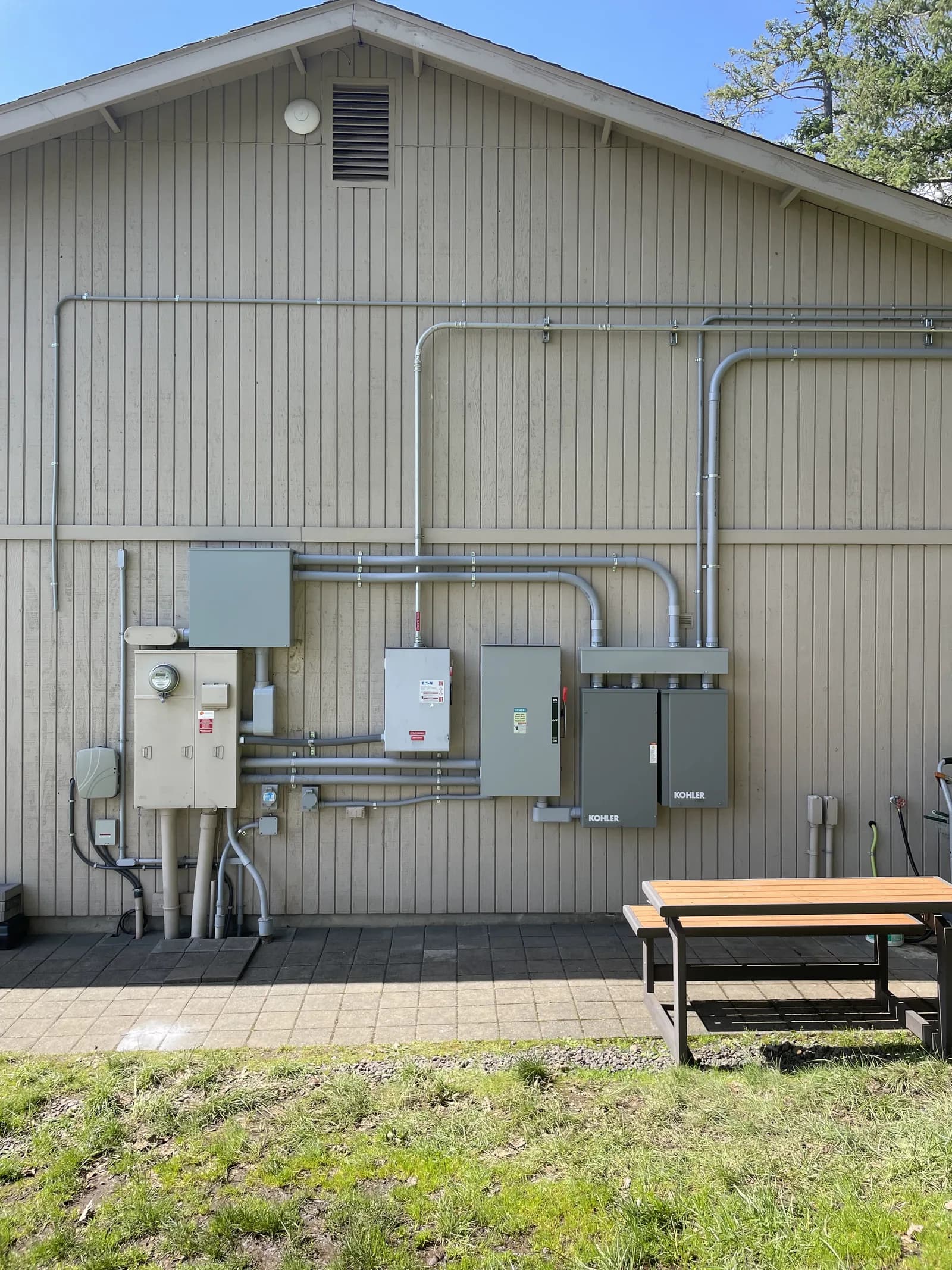 Service equipment across an exterior wall — meter, disconnects, load centre and a Kohler transfer switch joined by conduit