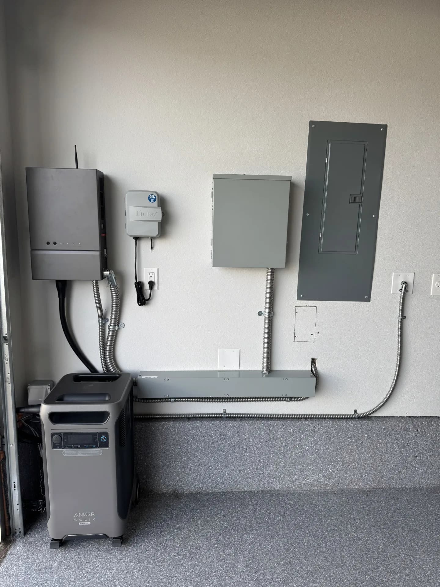 A garage wall with an inverter, disconnect, load centre and a portable battery unit below them