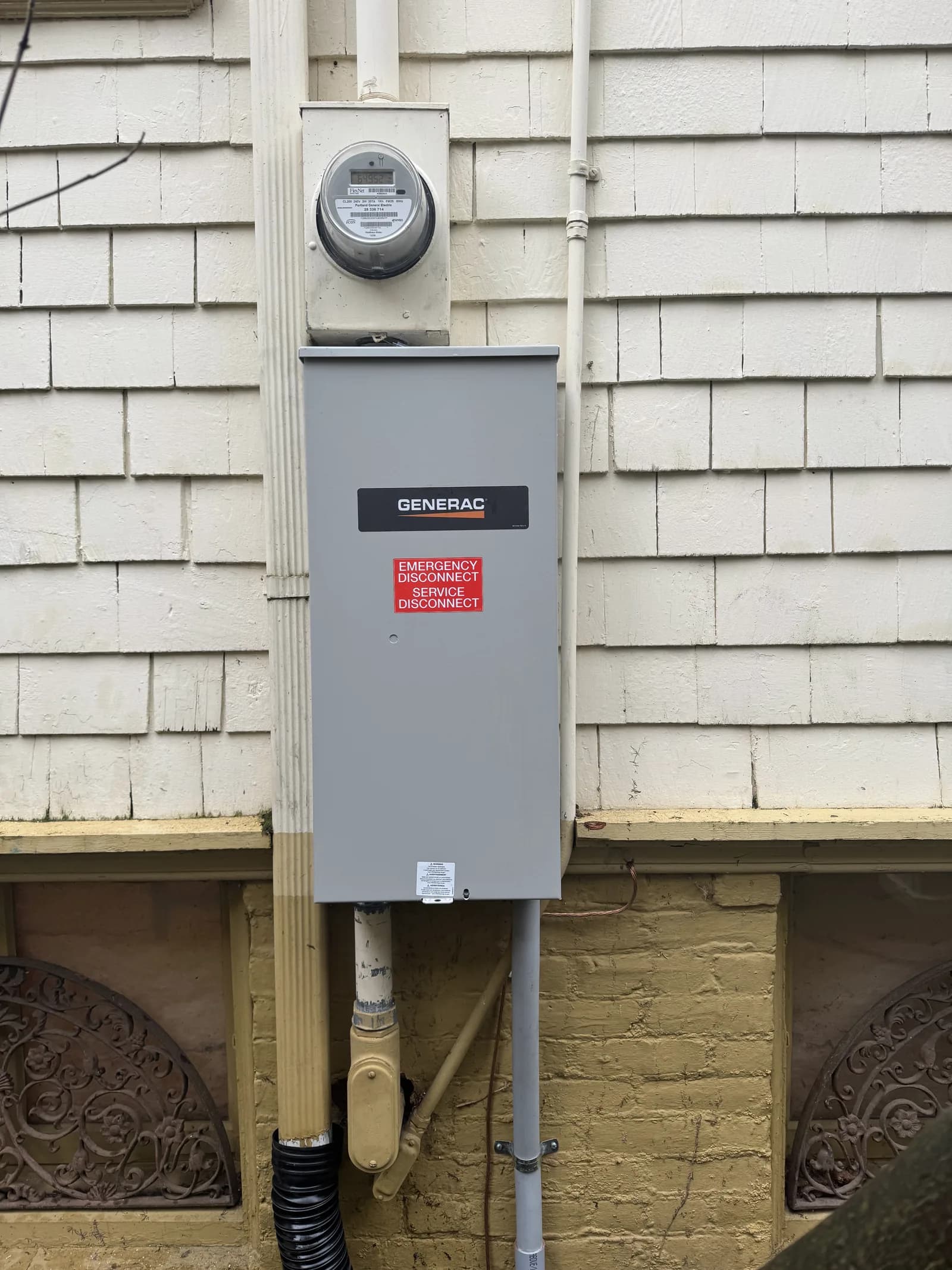 A Generac service disconnect under the meter on a shingled wall, conduit dropping to the crawlspace