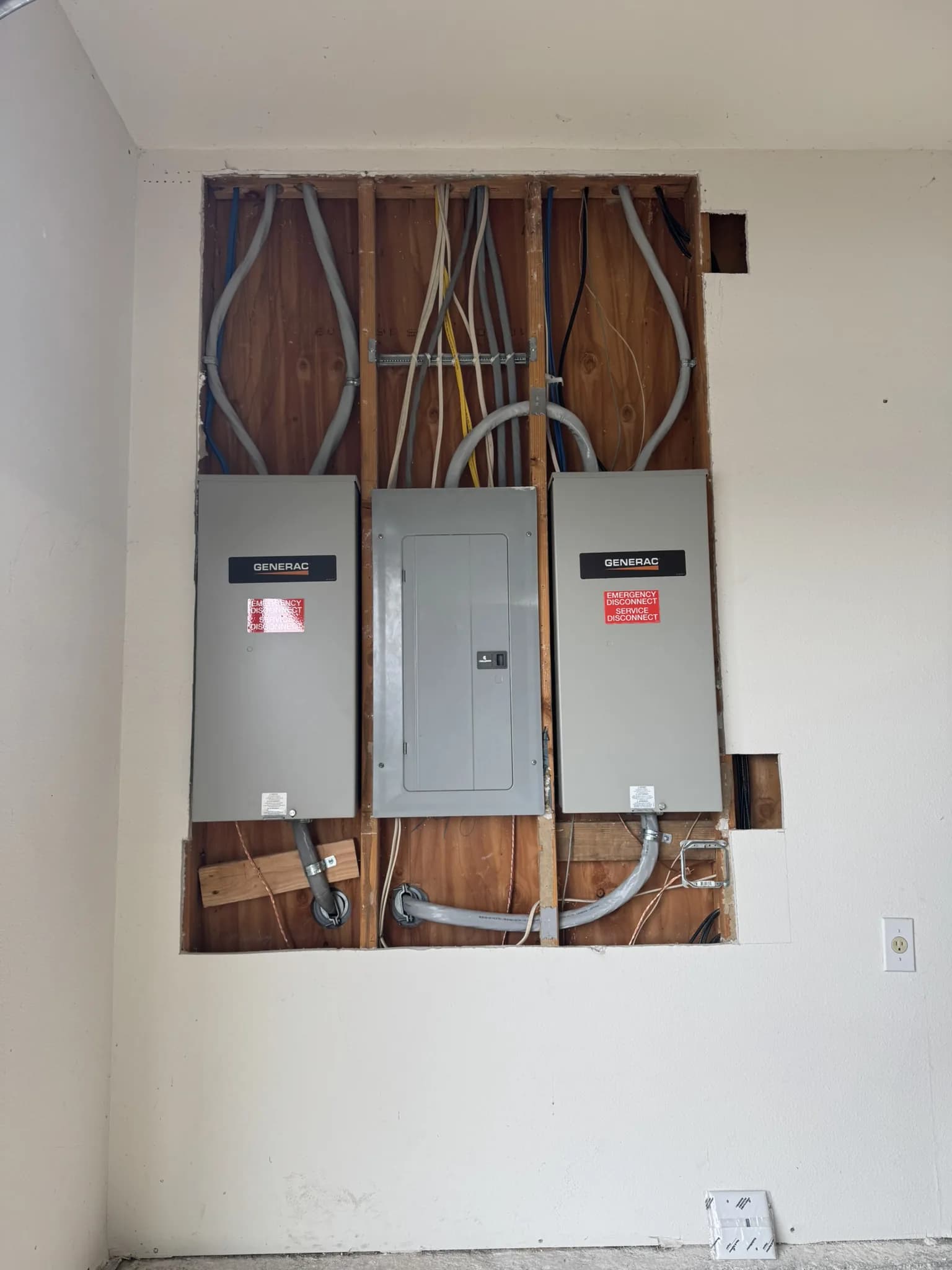 Two Generac transfer switches and a load centre in an opened wall, feeders run across the studs