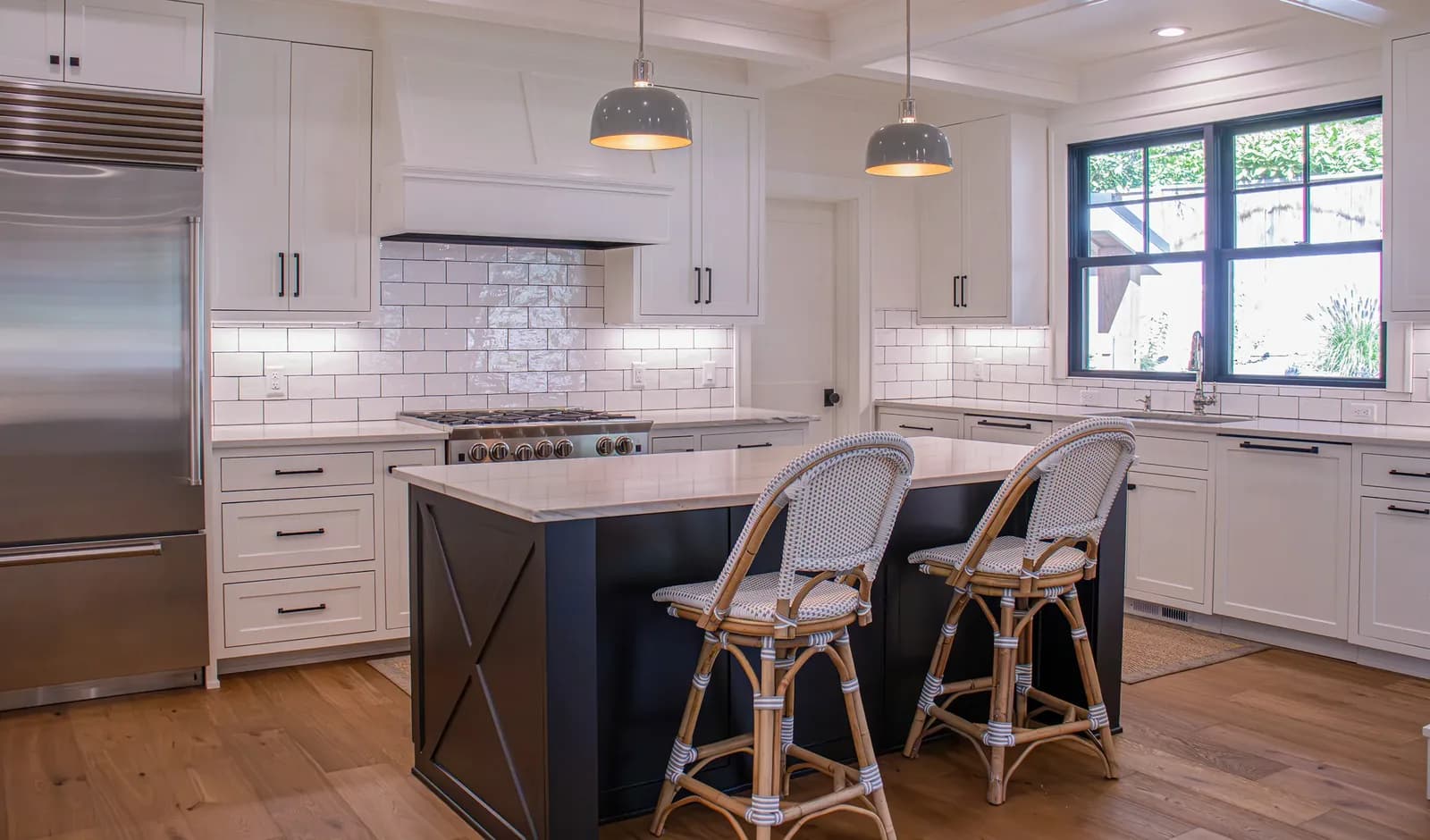 A white kitchen with two dome pendants over a navy island, undercabinet lighting along a subway-tiled backsplash
