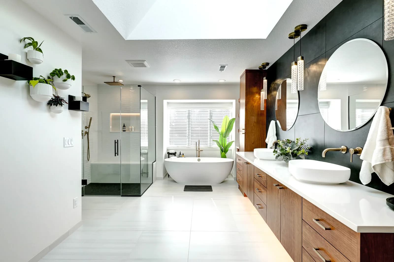 A primary bathroom lit by a skylight, pendant lights over a double vanity and a lit shower niche