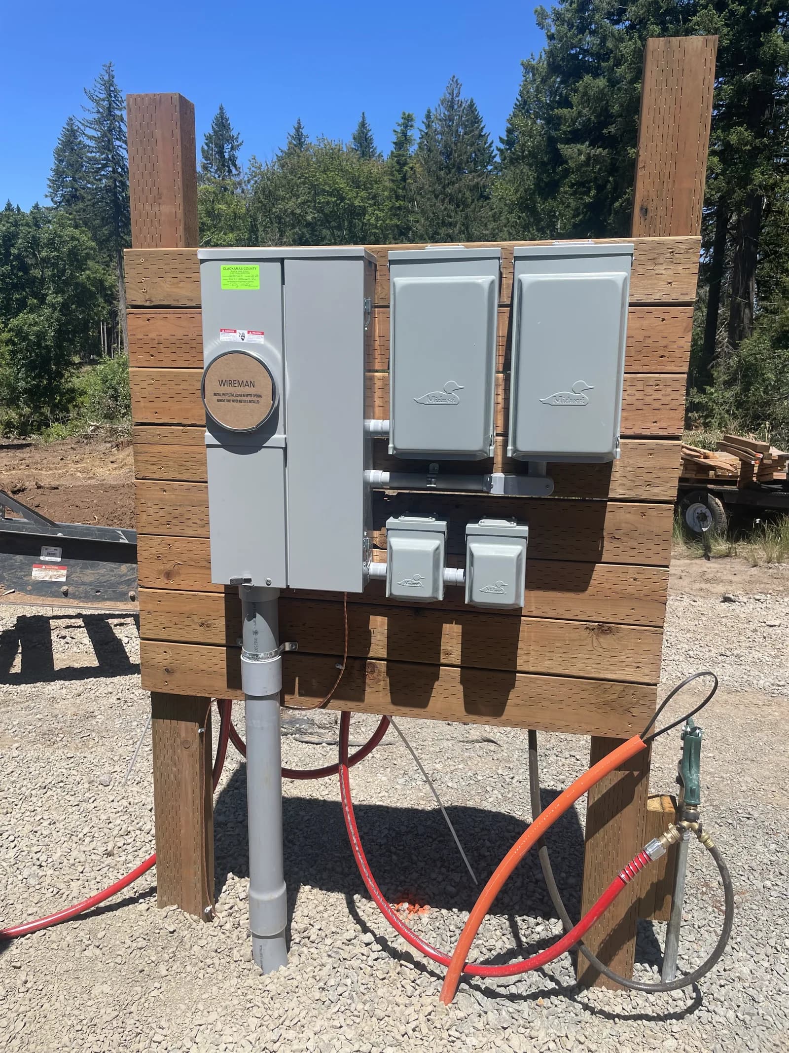 A temporary power pedestal on a cleared building site, meter and two disconnects on a timber frame
