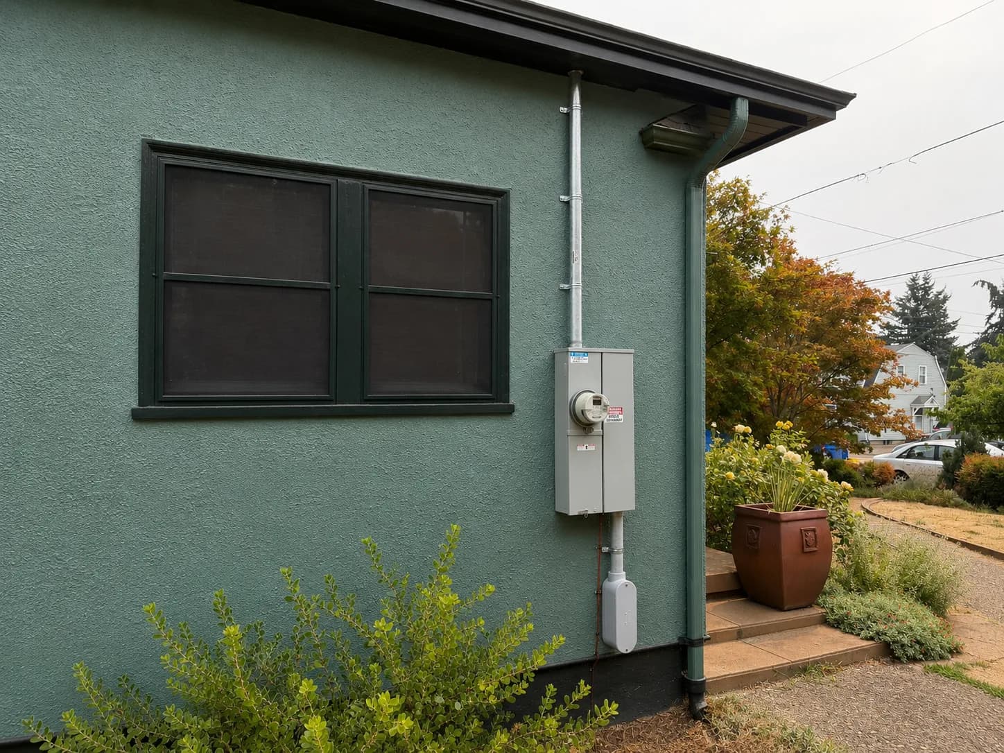 New meter base and service riser mounted on the stucco exterior of a green Portland house, with the mast run up to the roofline