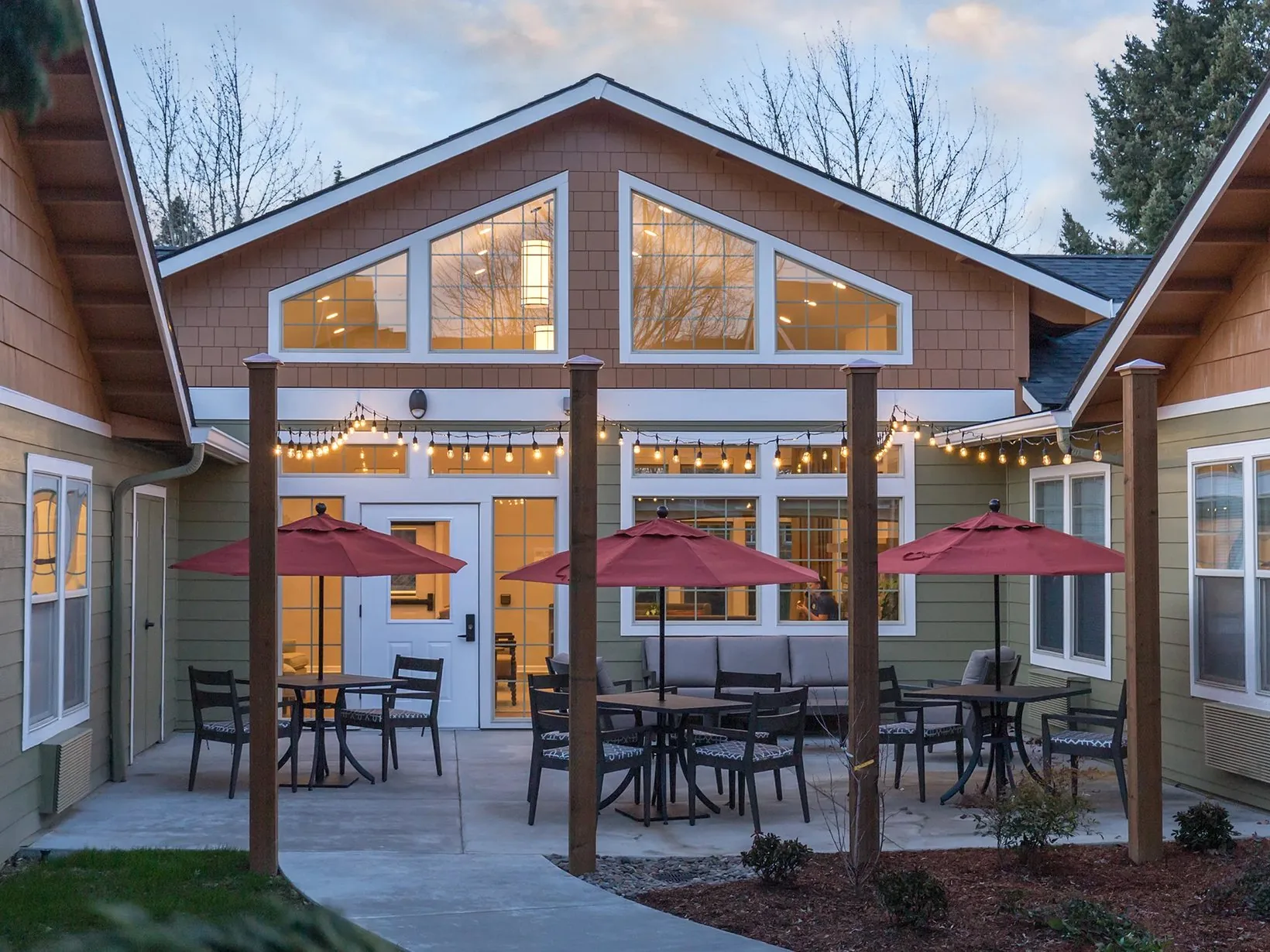A home exterior at dusk with the interior lights and patio string lighting switched on